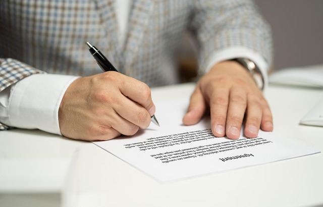 Close-up of a person signing a document with a black pen on a white desk.